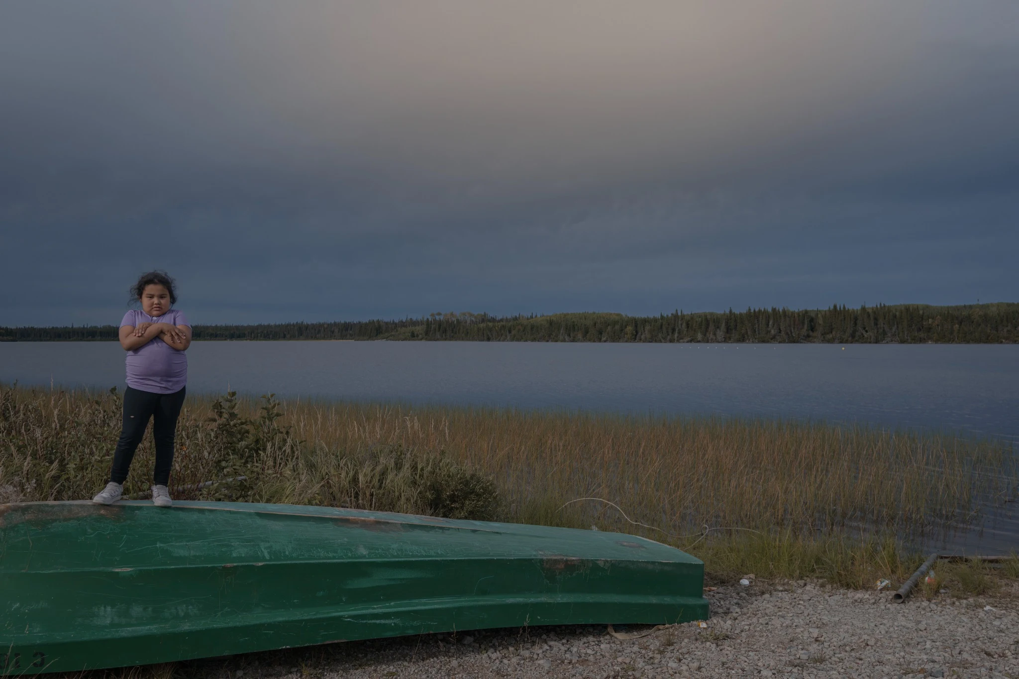 Girl standing on an overturned canoe by a lake