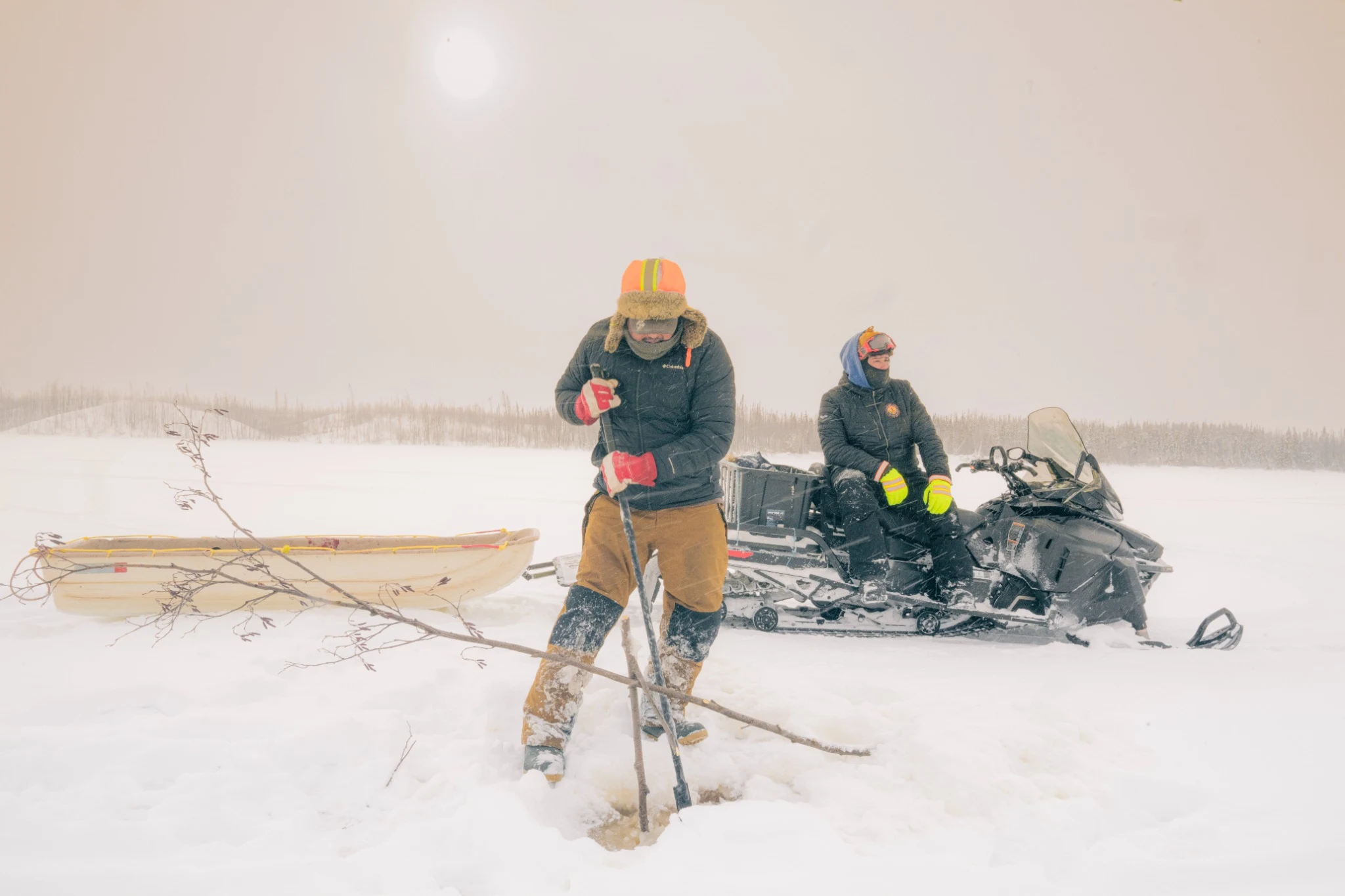 Travellers making a hole in the ice during blowing snow