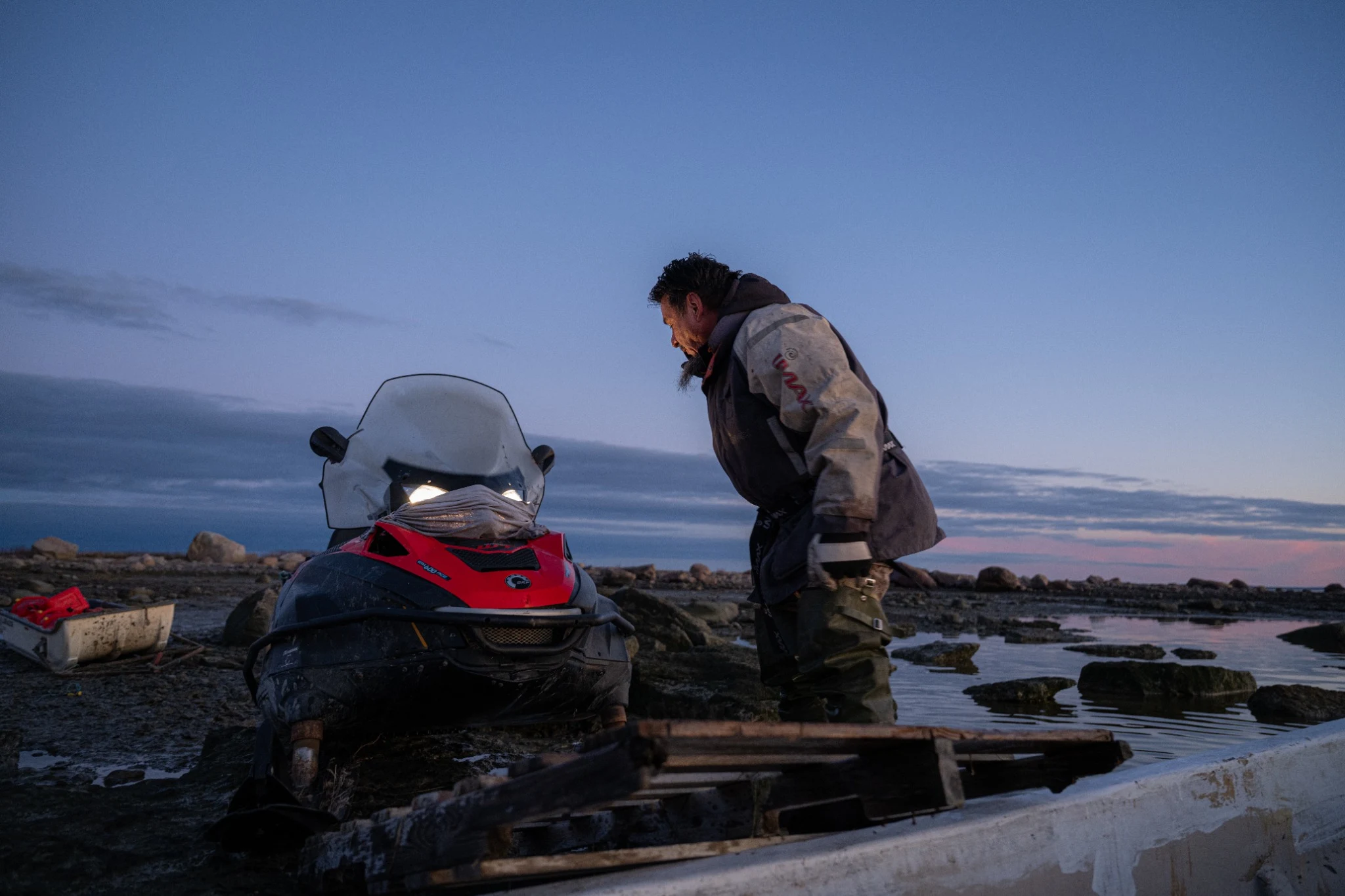 Man beside a snowmobile on the shore at dusk